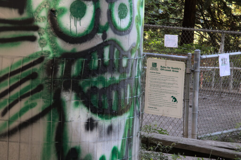 Picture of entrance to dog park also showing a scary face of graffiti on the way in