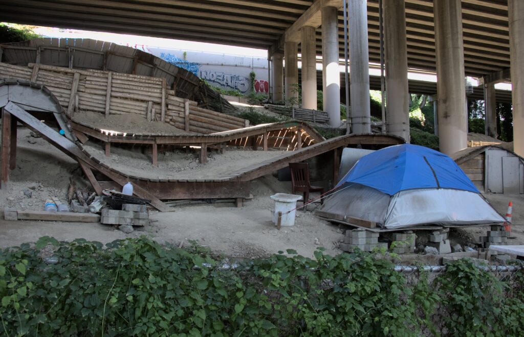 Dusty blue tent under I-5 highway with mountain bike ramps and columns behind it.